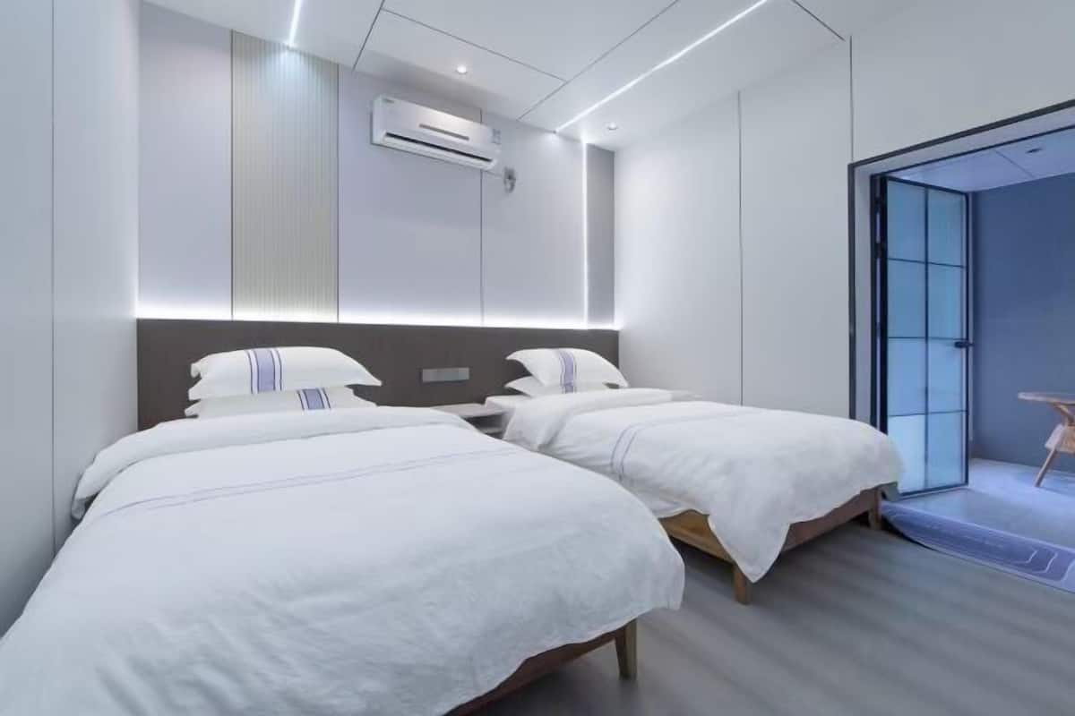 Een moderne hotelkamer met twee bedden, een ingebouwde airconditioning en een glazen deur naar een balkon.
