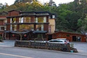 A traditional multi-story building with a balcony, a car parked in front, and a stone wall. - Xiaoxi Hostel (Zhangjiajie)