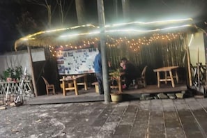 An outdoor seating area with tables and chairs, a covered section with string lights, and a poster on the wall.