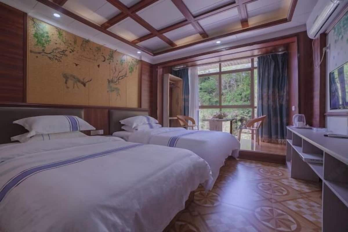 Een hotelkamer met twee bedden, een groot raam met uitzicht op groen, een houten plafond en een kaart aan de muur.