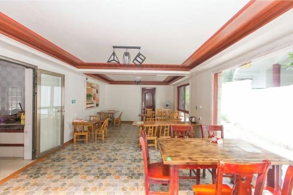 A dining area with a large wooden table and chairs, a patterned floor, and a view through a glass door.