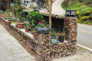 A stone planter with potted plants and a small tree, located beside a road.