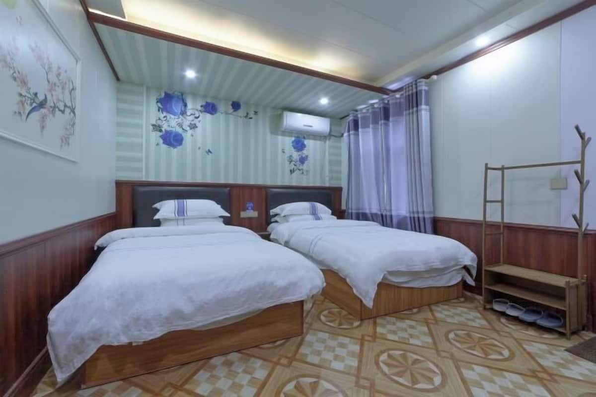 Een kamer met twee bedden, een houten hoofdbord, een kamer met een patroon vloer, een luchtverkoeler aan de muur en een gordijn.