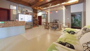A spacious living area with a wooden ceiling, a reception desk, a television, and a dining area. - Xiaoxi Hostel (Zhangjiajie)