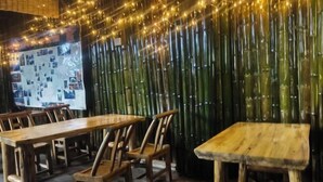 A restaurant with bamboo walls, wooden tables and chairs, and string lights. - Xiaoxi Hostel (Zhangjiajie)