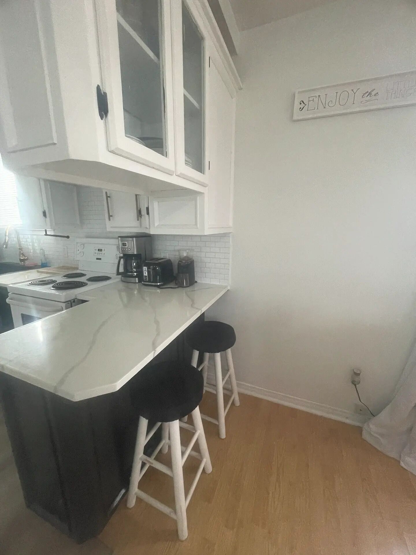 A kitchen with white cabinets, a white countertop, a coffee maker, a toaster, and two black stools.