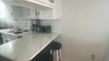 A kitchen with white cabinets, a white countertop, a coffee maker, a toaster, and two black stools.