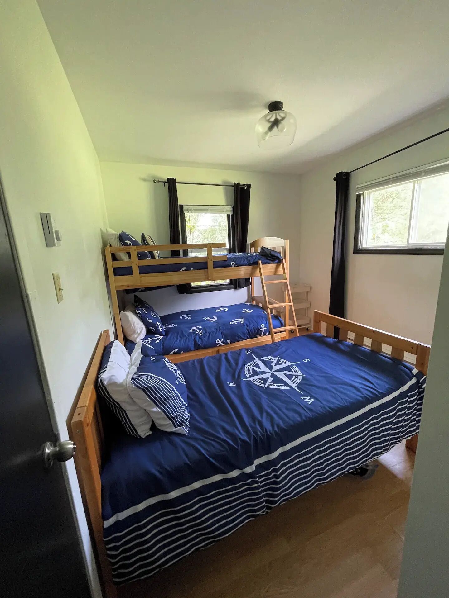 Una habitación individual con una cama nido, una ventana con cortinas, un ventilador de techo y una puerta.
