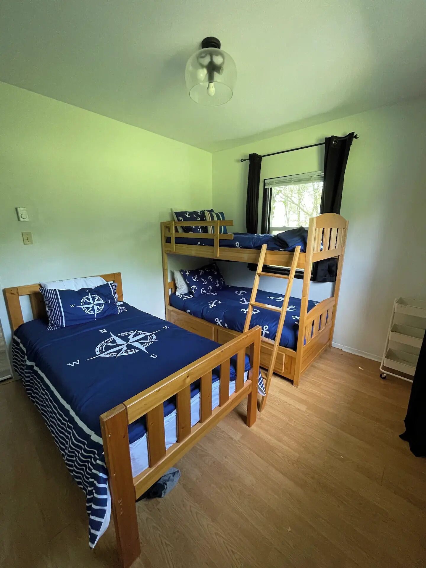 Een kamer met stapelbedden, een plafondlamp, een raam met gordijnen en een radiator.