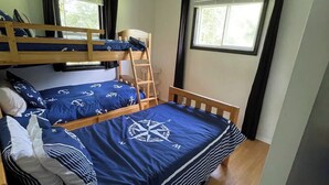 Habitación con literas, un edredón con diseño de brújula, una ventana con cortinas y un ventilador de techo.