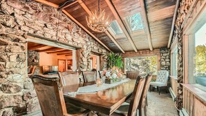 A rustic dining area with a stone wall, wooden ceiling, and a chandelier. - Historic Stone Mountain Lodge with Private Pond - convenient and secluded (Conifer)