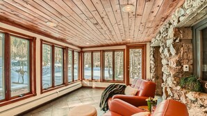 A cozy room with a stone wall, large windows, and a leather sofa. - Historic Stone Mountain Lodge with Private Pond - convenient and secluded (Conifer)