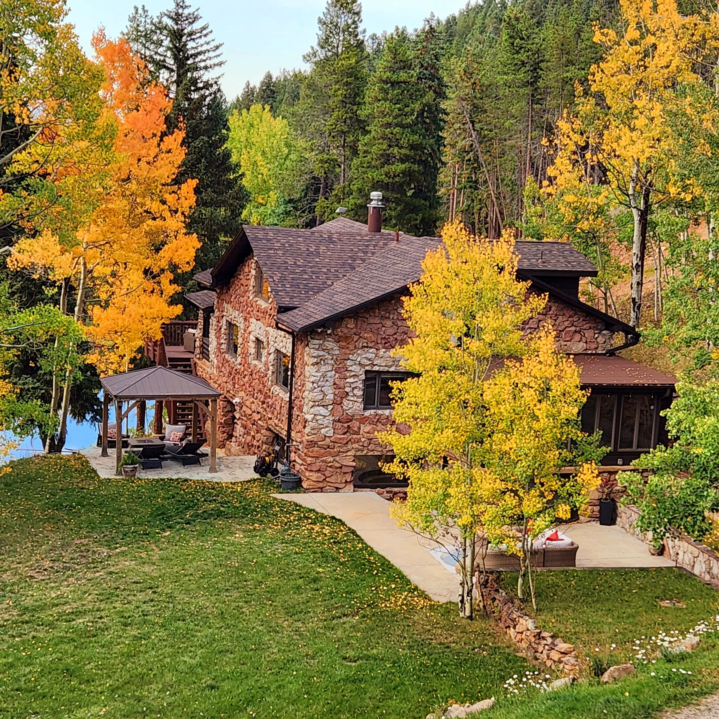 Une maison en pierre avec une cheminée en pierre, un patio couvert et une vue sur un lac.