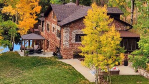 A stone house with a stone chimney, a covered patio, and a view of a lake. - Historic Stone Mountain Lodge with Private Pond - convenient and secluded (Conifer)