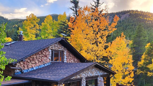 A stone cabin with a deck, surrounded by autumn foliage and a mountainous backdrop. - Historic Stone Mountain Lodge with Private Pond - convenient and secluded (Conifer)