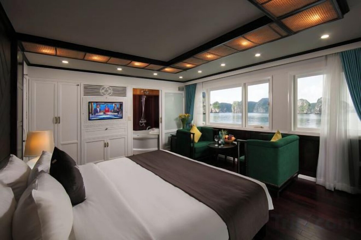 Habitación de hotel con una cama grande, televisión, zona de estar con mesa y vistas al exterior.