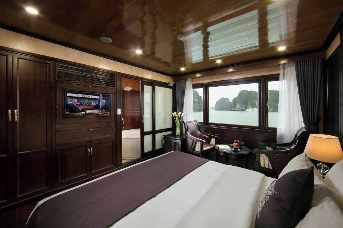 A hotel room with a large bed, a television, a desk with a chair, and a view of the sea.
