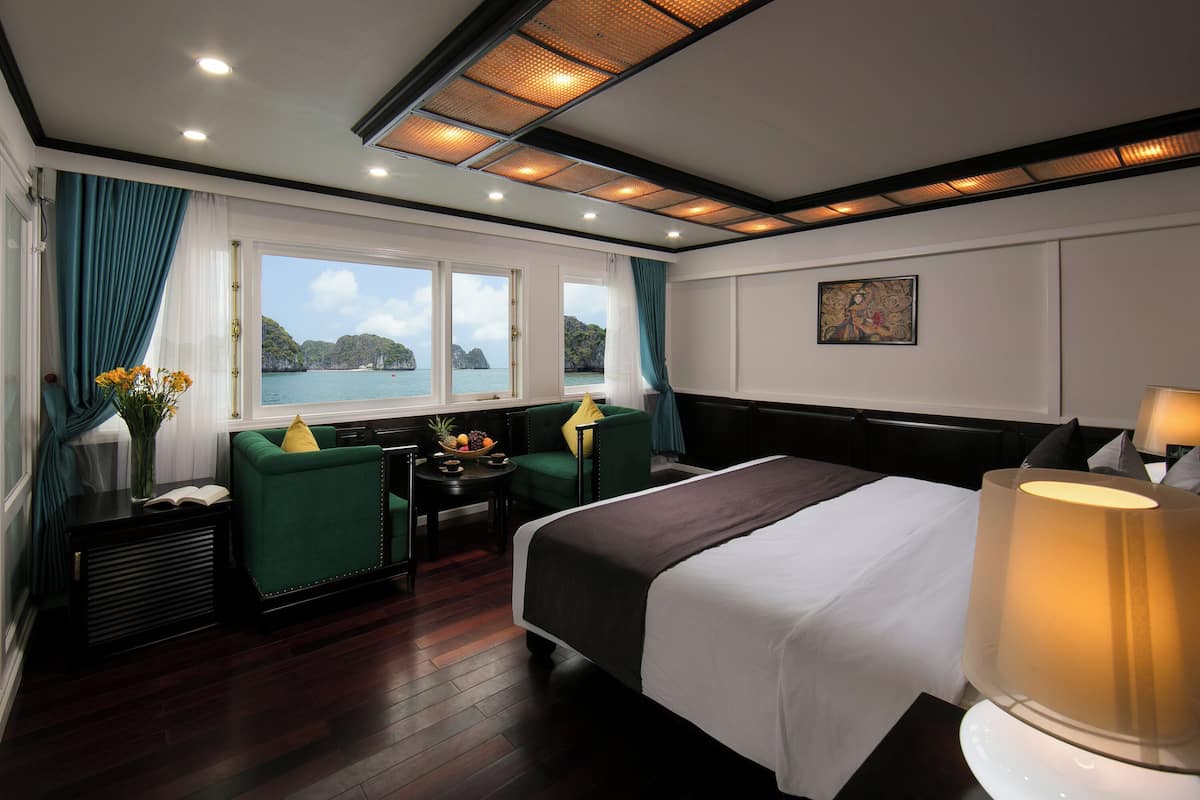 Habitación de hotel con cama, escritorio, dos sillas, ventana con vista al mar y un cuadro en la pared.