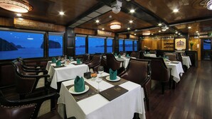 A restaurant with tables set for dining, large windows with a view of the sea, and a wooden ceiling. - La Regina Royal Cruise (Ha Long)