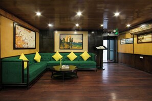 A hotel lobby with a green sofa, a round coffee table, and a painting of sailboats. - La Regina Royal Cruise (Ha Long)