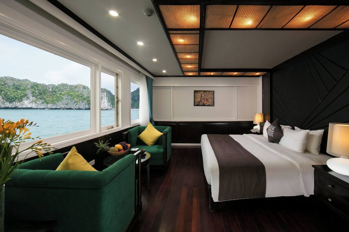 A modern hotel room with a large bed, a green armchair, a nightstand, and a view of the sea.