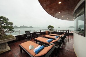A deck with lounge chairs, a table, and a potted plant. - La Regina Royal Cruise (Ha Long)