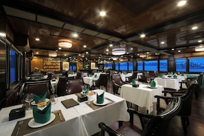 A restaurant with multiple tables, each set with white tablecloths, green napkins, and wine glasses.