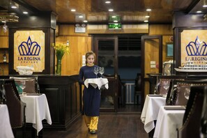 Interior de restaurante con paneles de madera, mesas con manteles blancos y un letrero que dice 'La Regina Cruises'.
