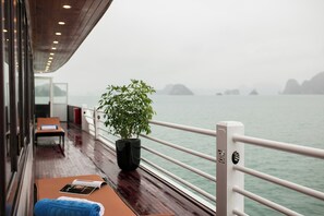 A deck with a potted plant, a table with a book, and a view of the sea. - La Regina Royal Cruise (Ha Long)