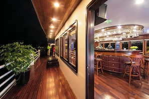 A bar area with wooden flooring and bar stools, a counter with a glass display, and a view of the deck outside.