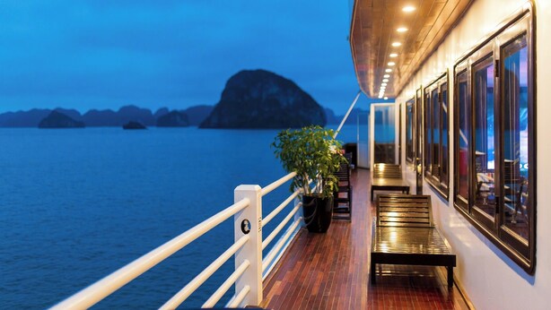 A balcony with a view of the sea and distant islands, a potted plant, and a bench. - La Regina Royal Cruise (Ha Long)