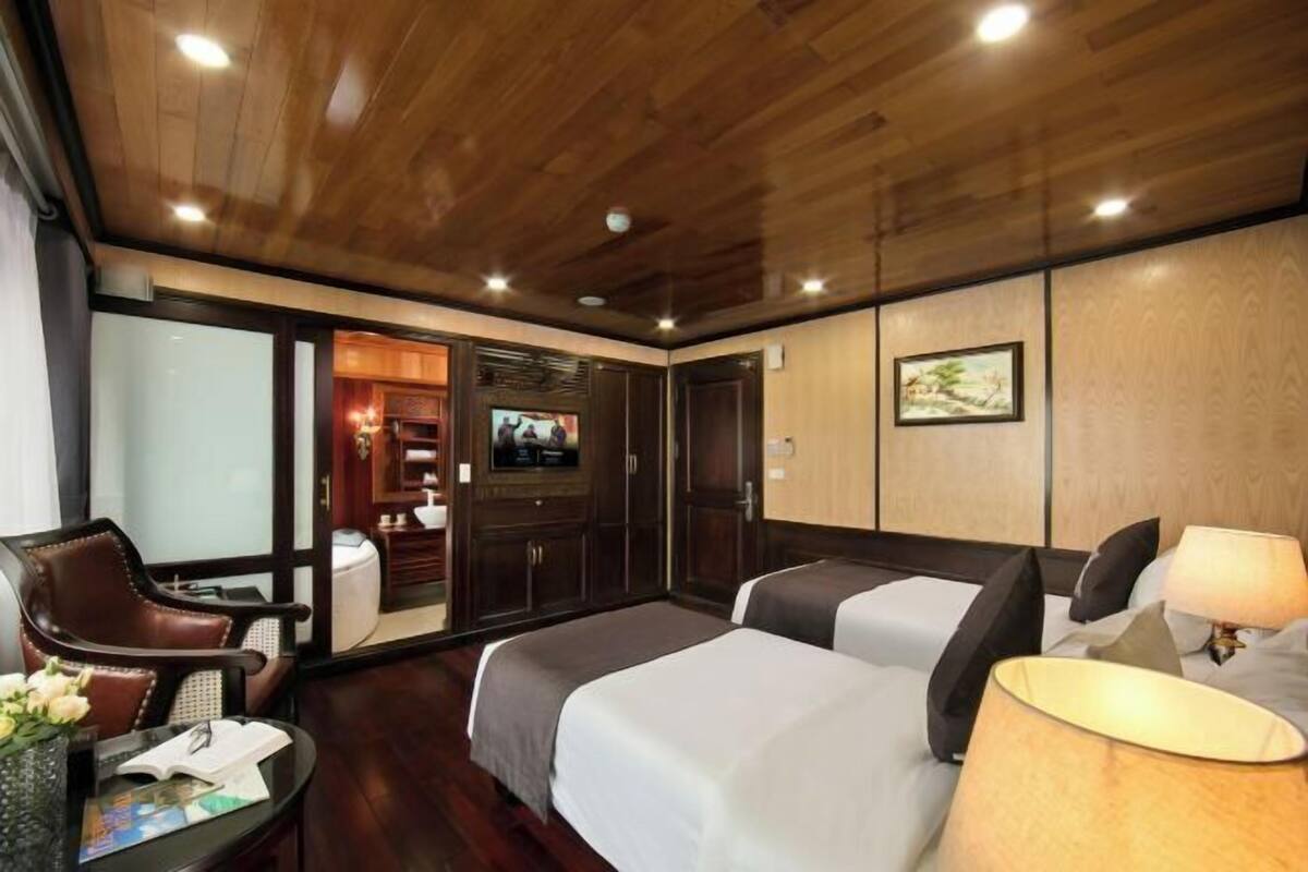 A hotel room with a wooden ceiling, two beds, a desk with a chair, a TV, and a painting on the wall.
