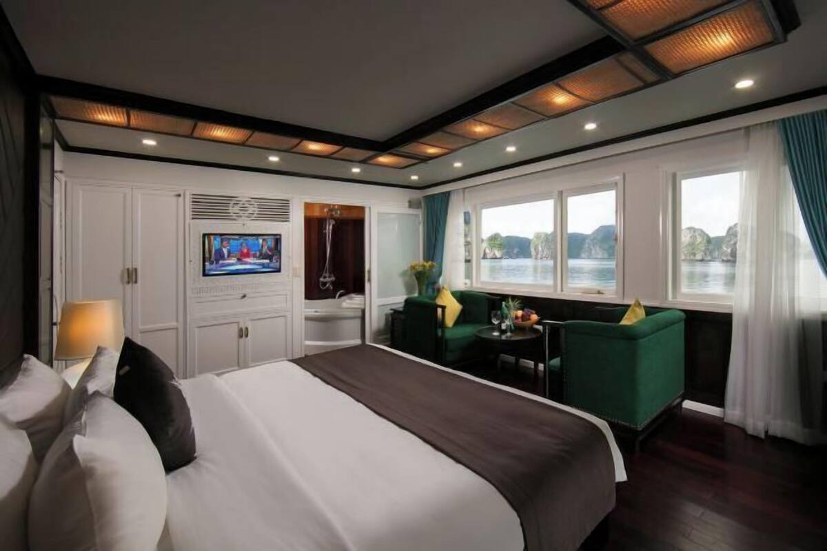 A hotel room with a large bed, a TV, a small table with chairs, and a view of the water.