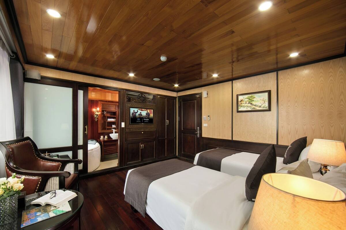 A hotel room with a wooden ceiling, a television, a bed, a desk with a lamp, and a chair.