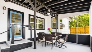A covered patio with a table and chairs, a blue door, and a wooden fence in the background.