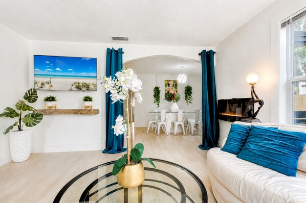 En moderne stue med en hvid sofa, et glasbord og et spiseområde med hvide stole.