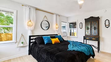 Une chambre à coucher avec un lit noir, des murs blancs, un ventilateur de plafond et une fenêtre avec des rideaux.