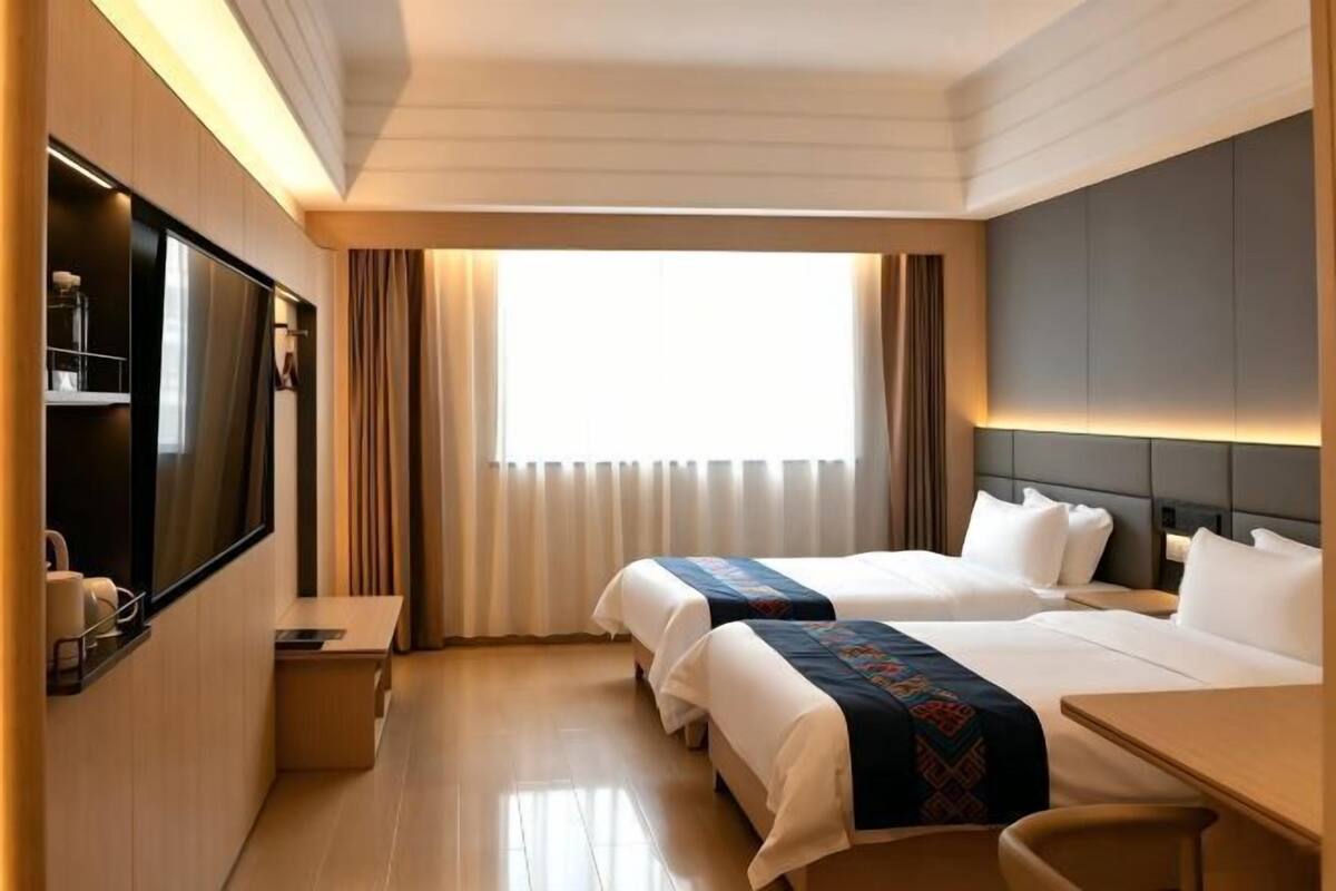 Habitación de hotel con dos camas, televisión, escritorio y ventana con cortinas.