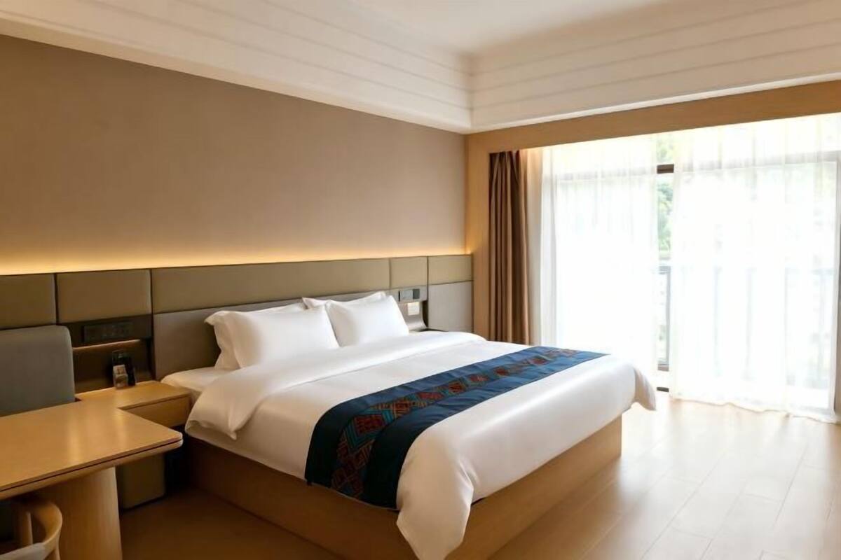 Una habitación de hotel con cama, mesita de noche y vistas al exterior.