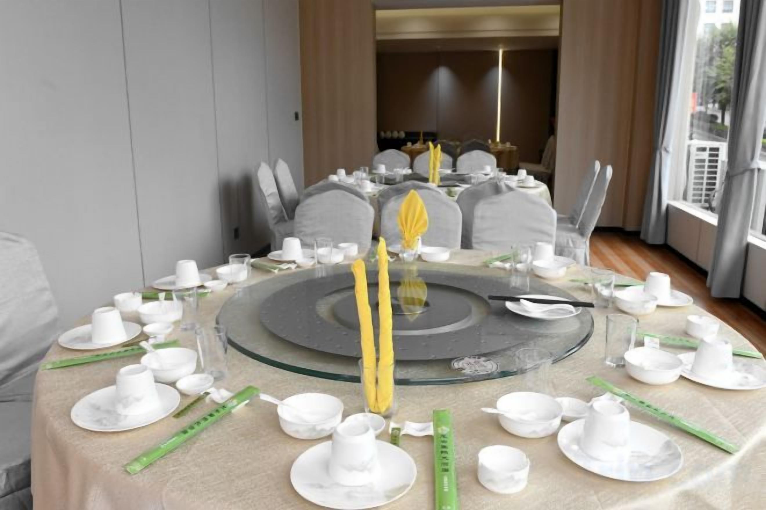A round dining table set with white plates, cups, and cutlery, with a central yellow candle.