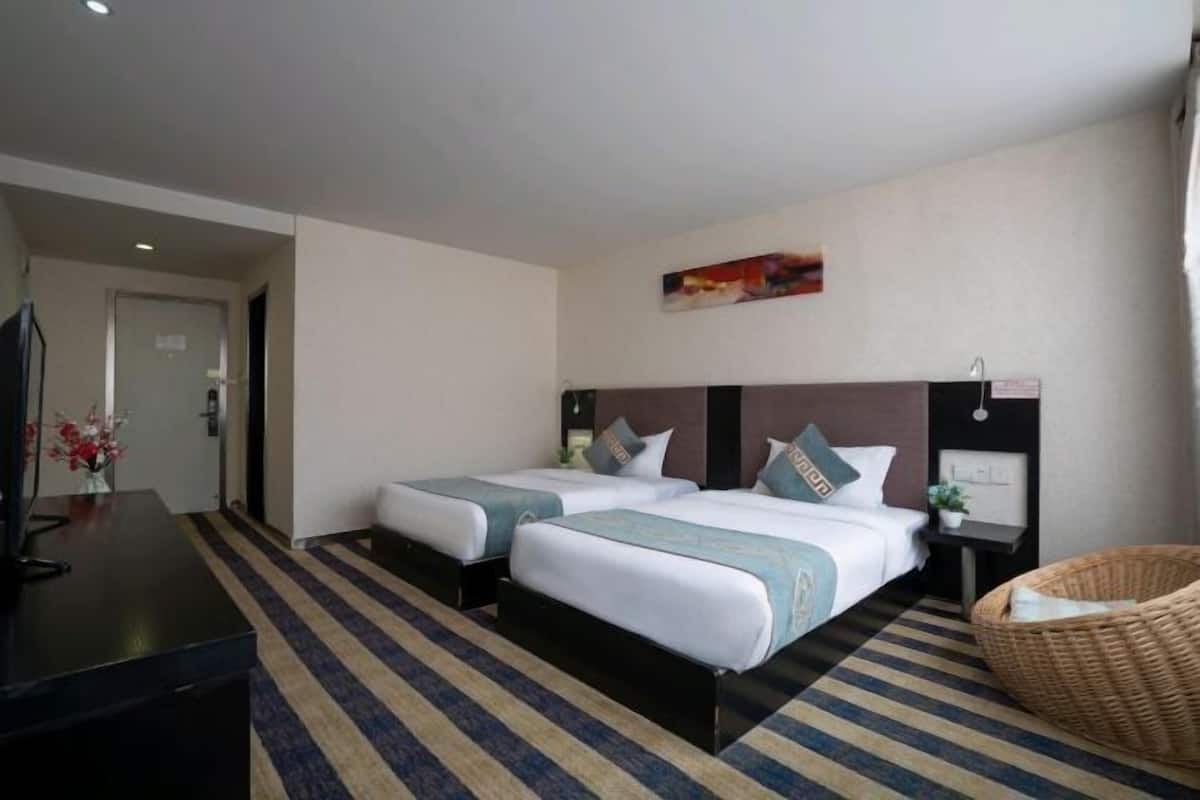 A hotel room with two beds, a television, a desk, and a wicker chair.