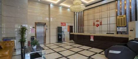 A hotel lobby with a reception desk, a waiting area with chairs, a reception desk, a staircase, and a wall-mounted air conditioning unit.