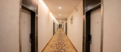 A hotel hallway with doors on both sides, carpeted with a floral pattern, and a ceiling light fixture.
