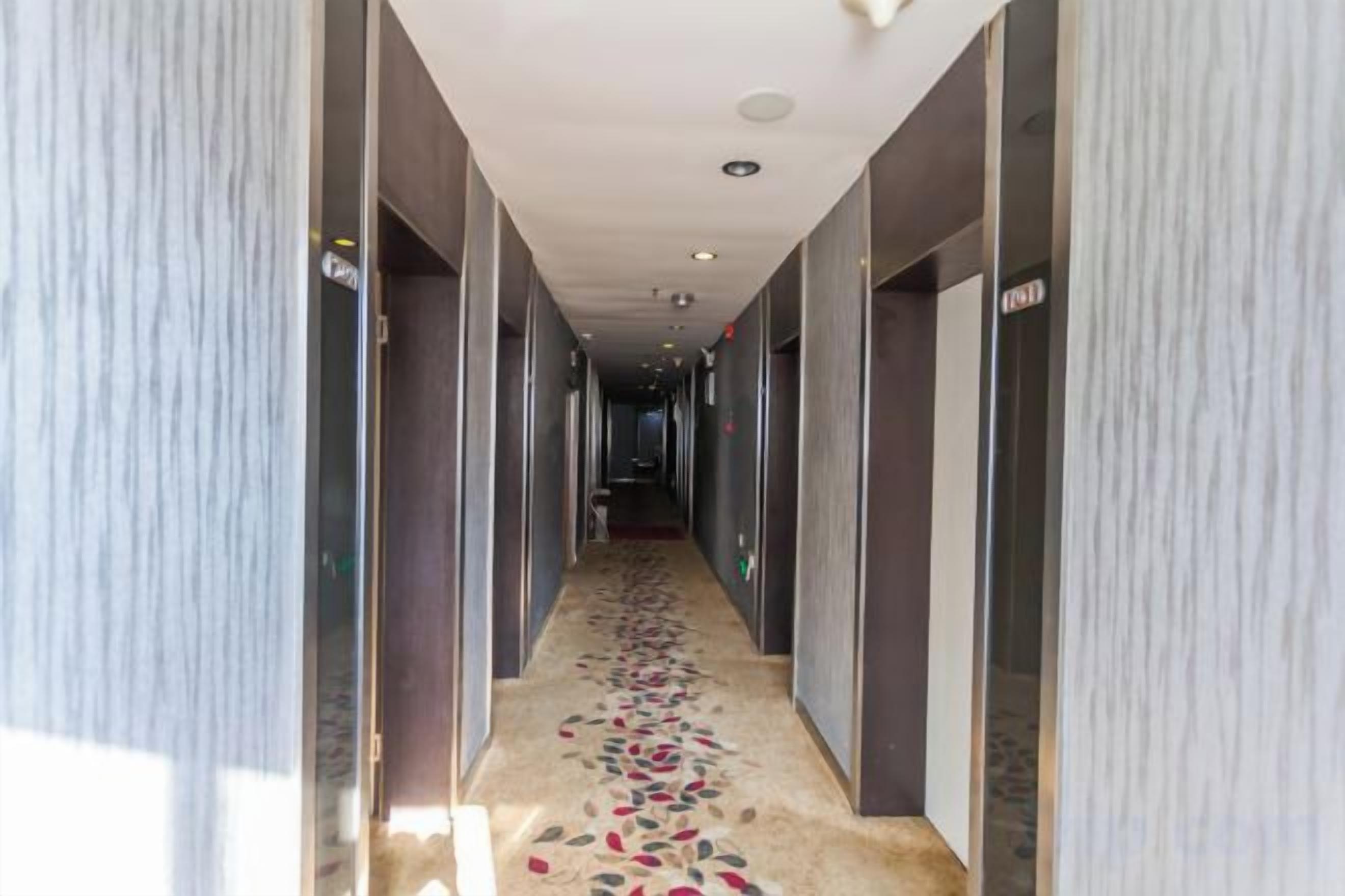 Corredor de hotel com carpete estampado, portas em ambos os lados e teto com iluminação embutida.