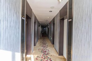 Ein Hotelkorridor mit gemustertem Teppich, Türen auf beiden Seiten und einer Decke mit eingelassenen Leuchten.