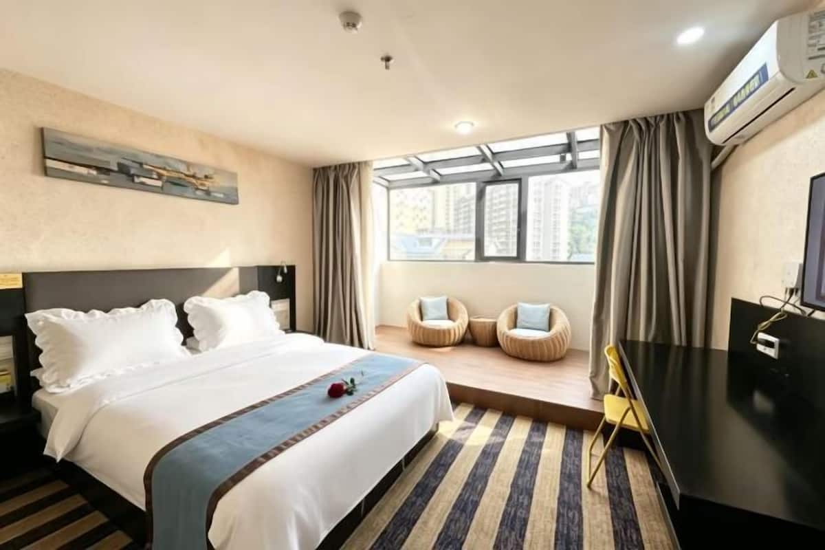 A hotel room with a bed, a desk, a chair, a TV, and a window with curtains.