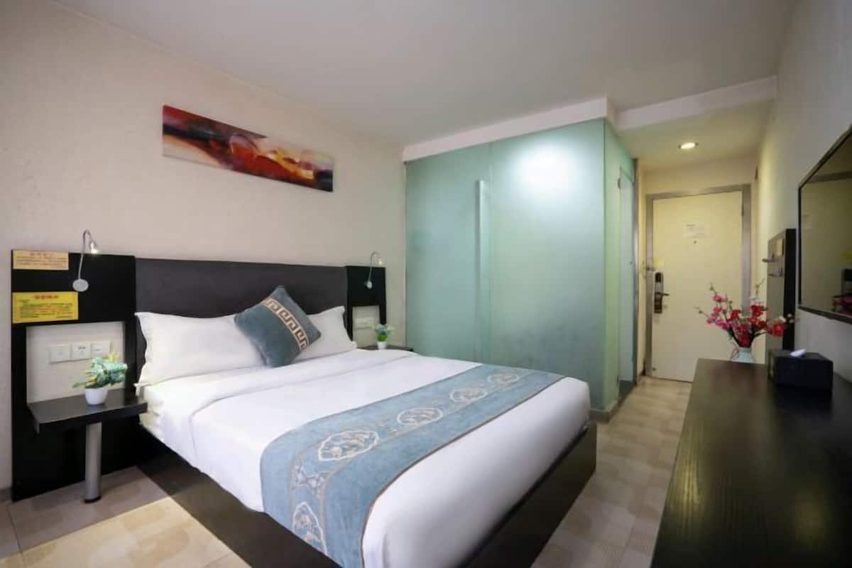A hotel room with a bed, bedside table, nightstand, and a door leading to another room.