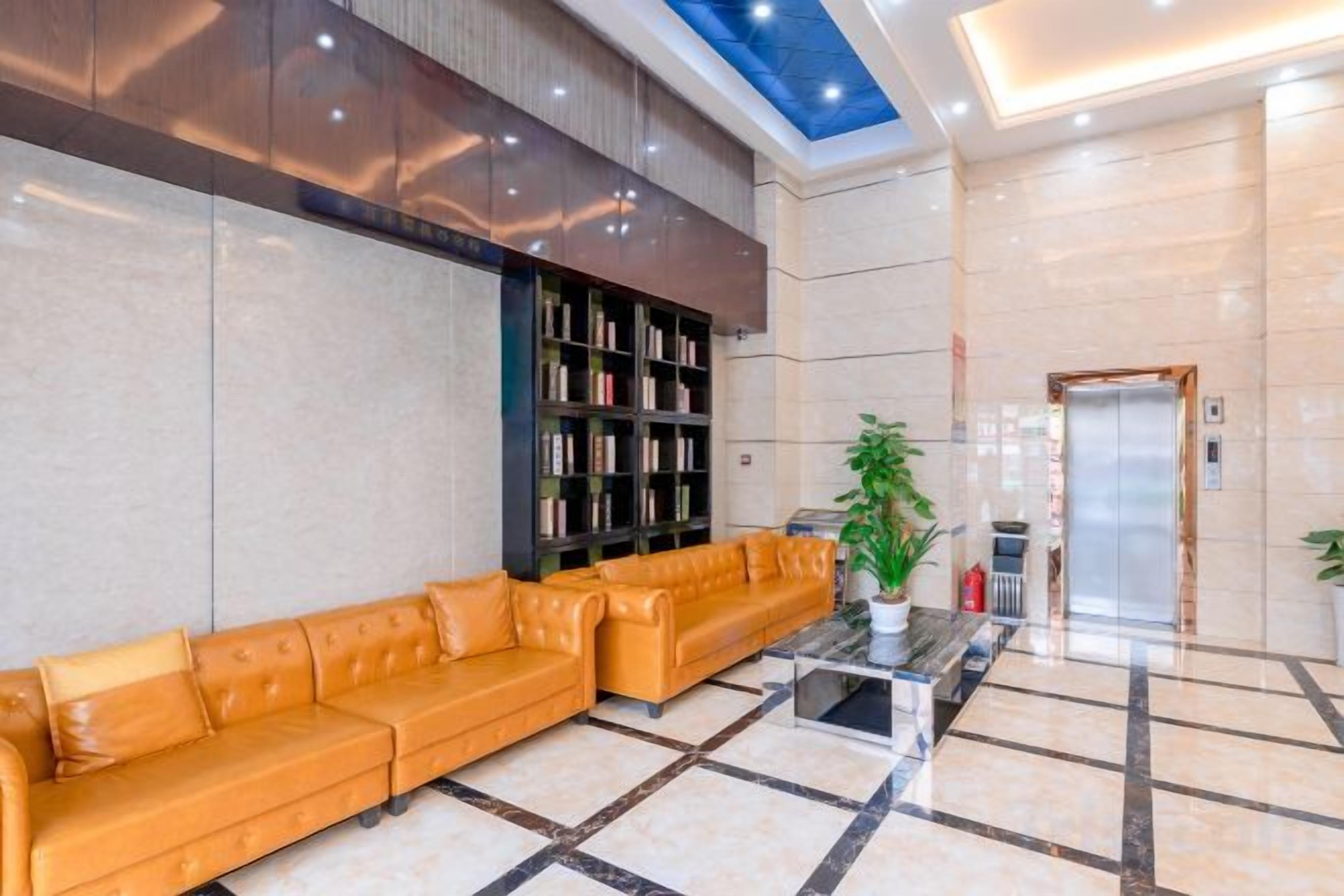 Um hall de hotel com sofá, estante de livros, mesa de centro e elevador.