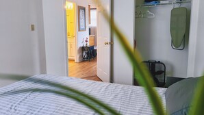 Une chambre avec un lit, une armoire où sont rangés des vêtements, et une vue sur la cuisine.
