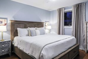 A neatly made bed with a wooden headboard, a bedside table with a patterned drawer, and a window with curtains. - Perfect for Groups! Near Forsyth w/Yard & Parking! (Savannah)